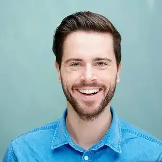 Smiling man in a blue shirt with a neatly groomed beard posing against a light blue background for an author website