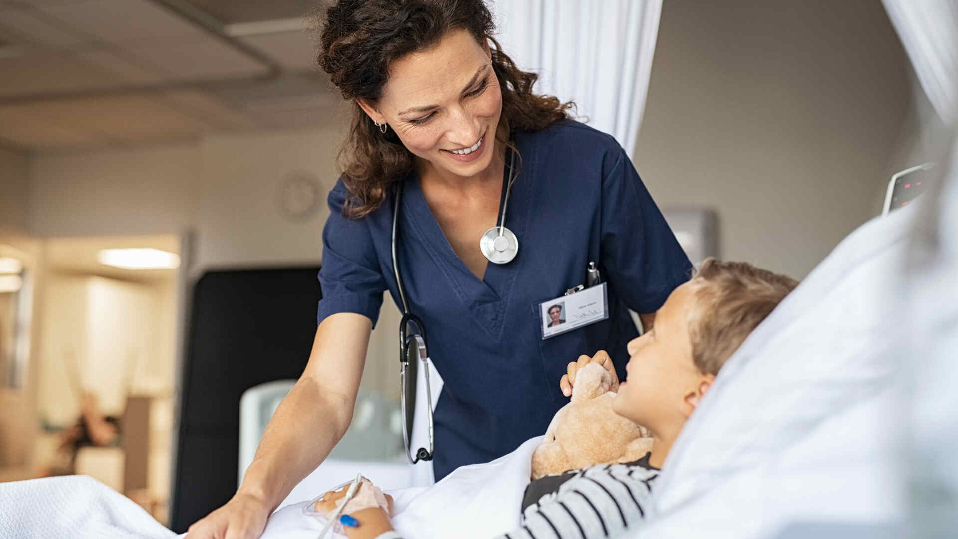 Smiling nurse caring for a young patient in a hospital bed while providing compassionate Pediatric healthcare support